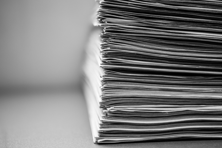 Newspapers stacked neatly in a tall pile, isolated on blurred white background.