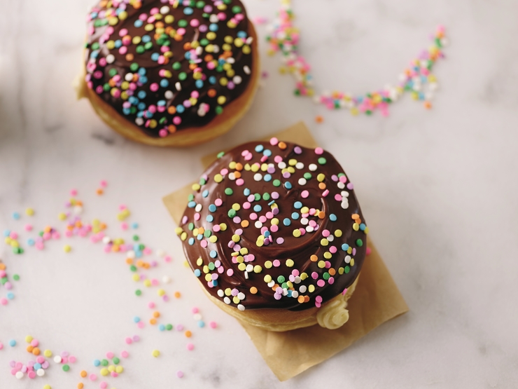Two chocolate-frosted "cake batter" doughnuts topped with sprinkles on marble counter.