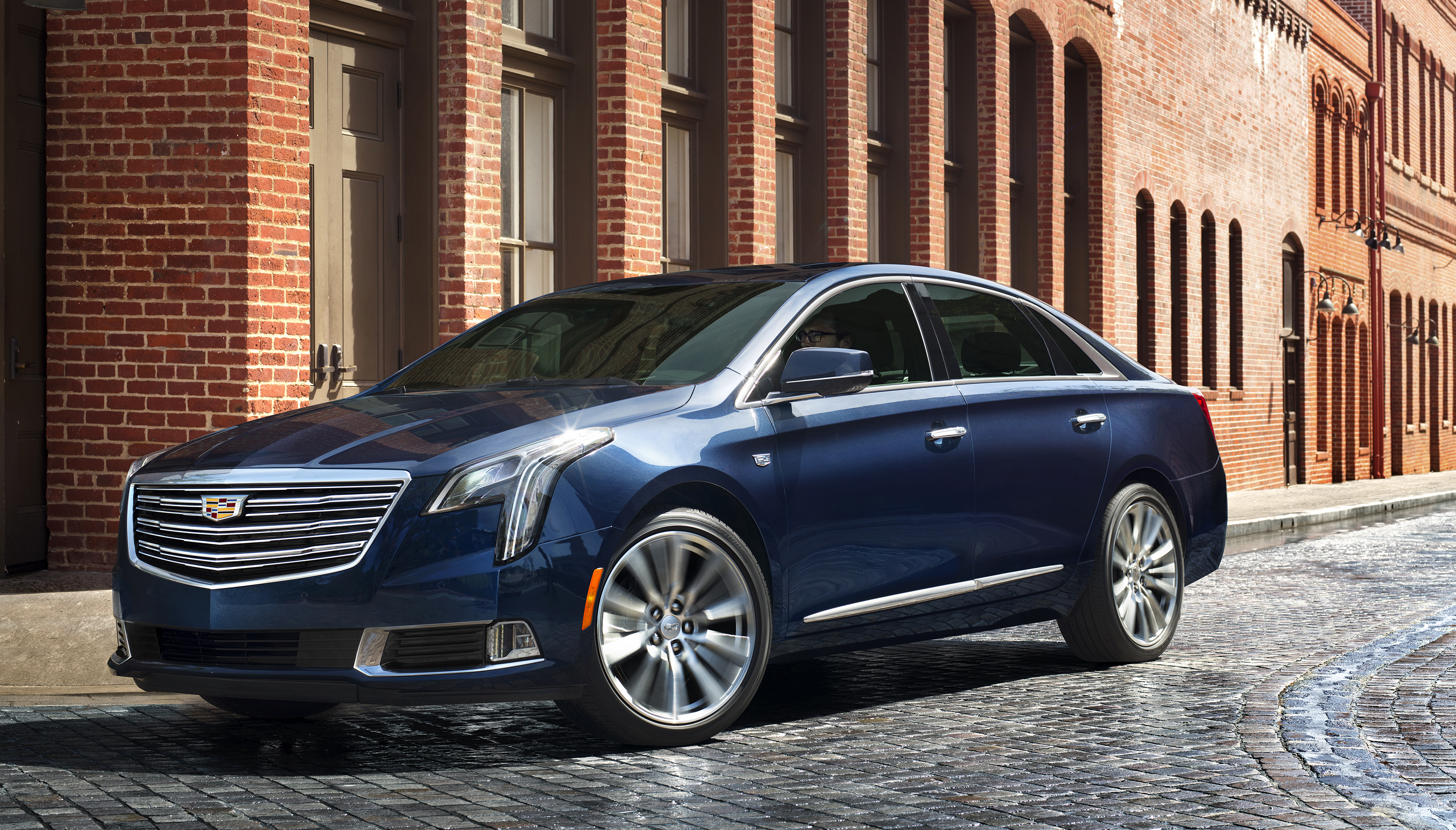 A dark blue Cadillac XTS sedan parked on a cobblestone city street.