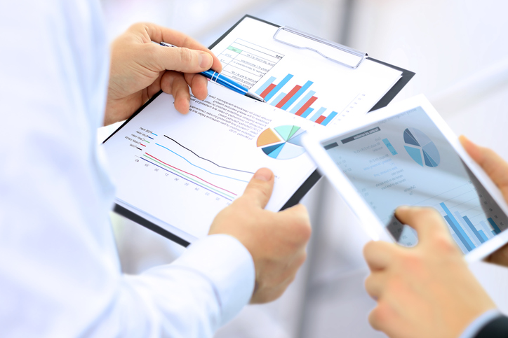 Two business colleagues analyzing colorful financial statements in hard copy and on tablet.