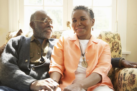 Senior man and woman sitting on couch holding hands and smiling