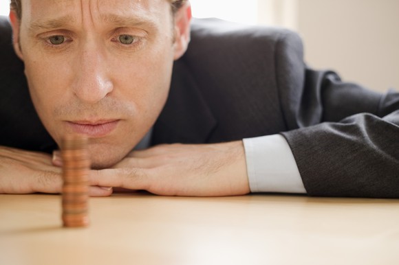 A depressed man in a suit staring at a single stack of pennies on a table.