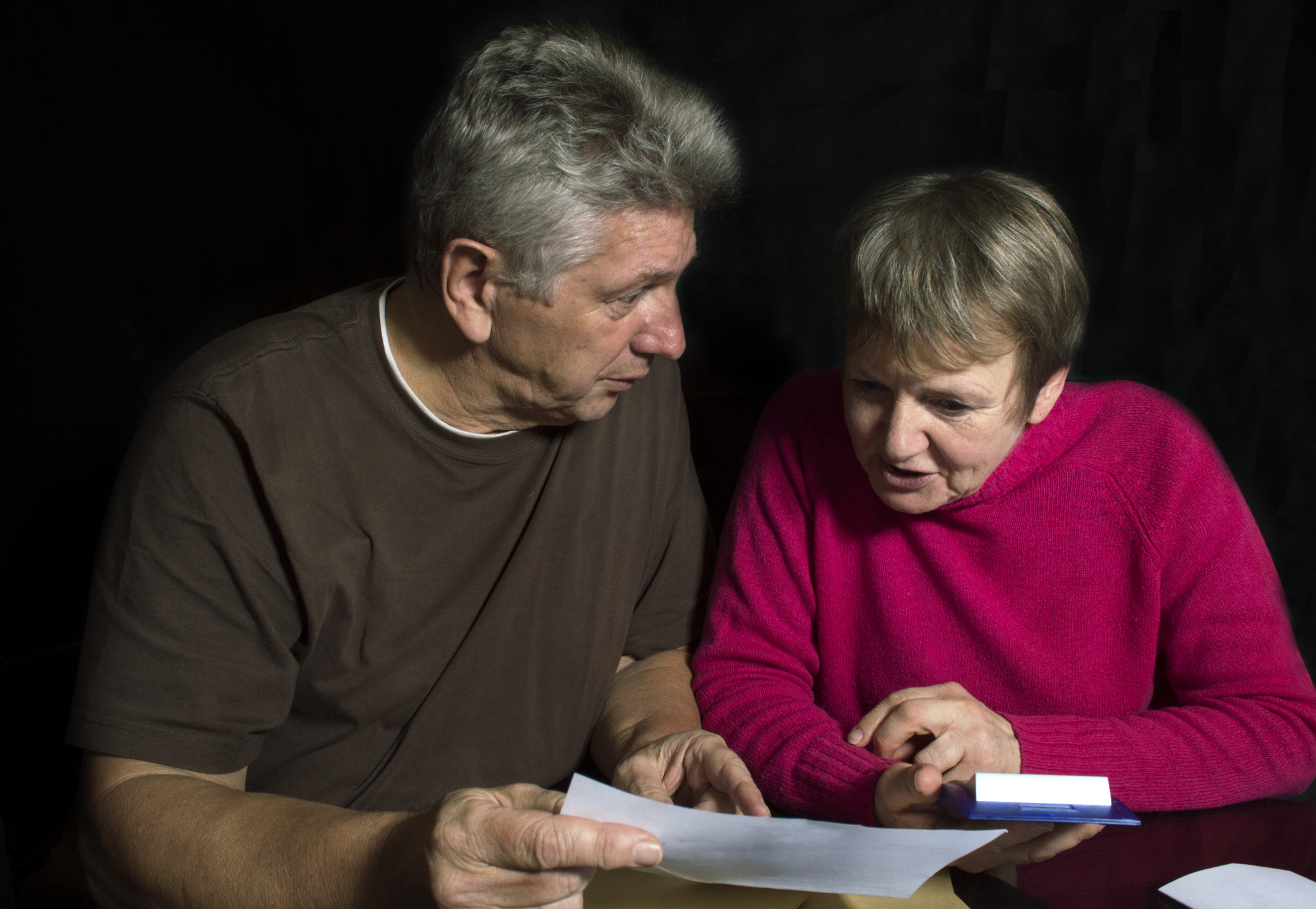 A senior man and woman sitting side by side, reviewing a piece of paper.