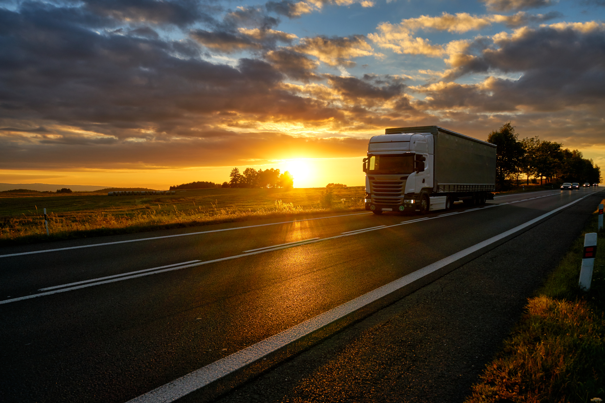 Tractor trailer truck driving down road at sunset