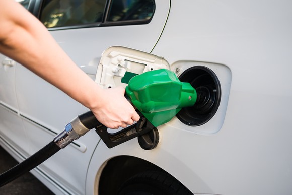 A hand holding a green diesel pump to refuel a white vehicle.