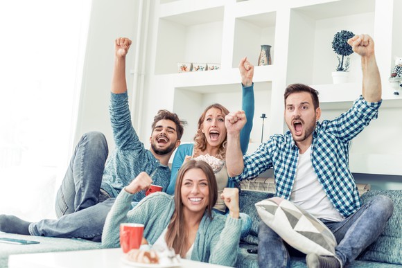 Four friends on a couch, cheering while watching a sporting event.
