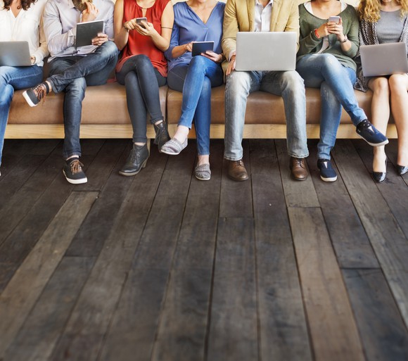 People sitting on a couch, using their laptops and smartphones.