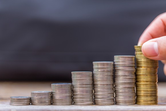 Stacks of coins ascending in size from right to left, with a person placing a coin on the largest stack.