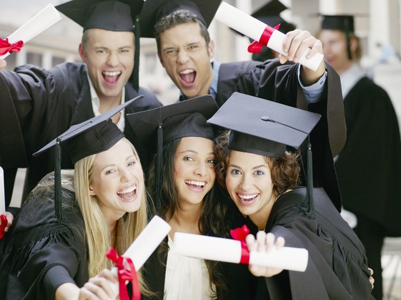 Jubilant college students in caps and gowns holding their college diplomas.