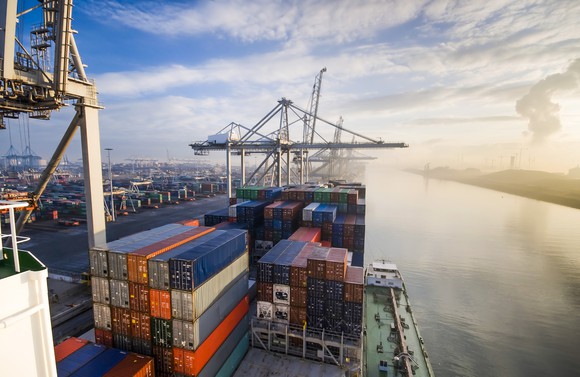 Shipping containers on a ship at port with the sun rising in the background.