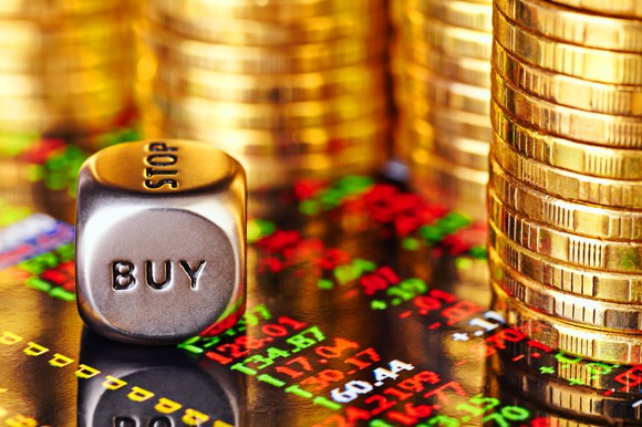 Stacks of gold coins beside a die showing the word buy.