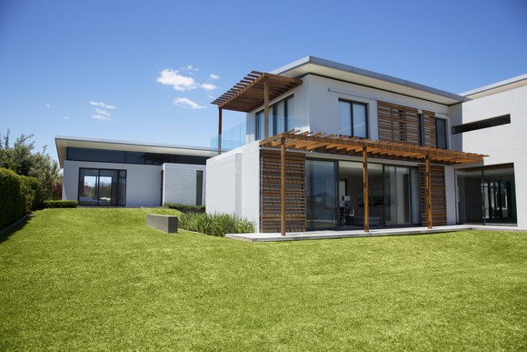 White two-story modern home with white walls and wood accents, and a green grass lawn.