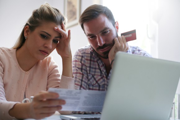 Woman looking concerned while holding a piece of paper and man looking concerned while holding a credit card