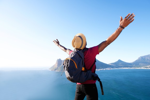 Man with backpack facing ocean and mountain scenery