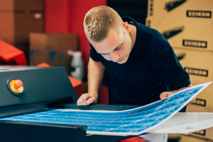 Young Man Looking at MakeReady Printing Sheets in a Print Factory