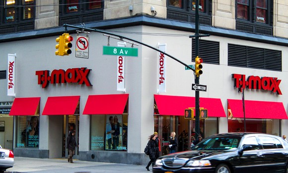 The outside of a TJ Maxx at an intersection in an urban setting. People and cars are passing by in the foreground.