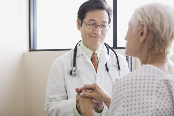 A smiling doctor holding the hand of sick patient.