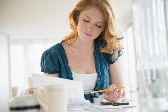 Woman with pencil staring at paper in brightly-lit kitchen.