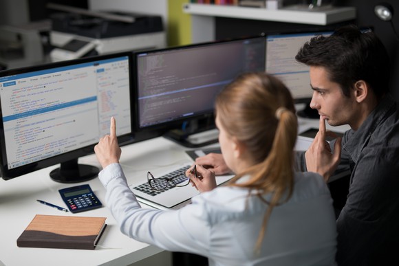 Two software engineers programming together on multiple computer screens