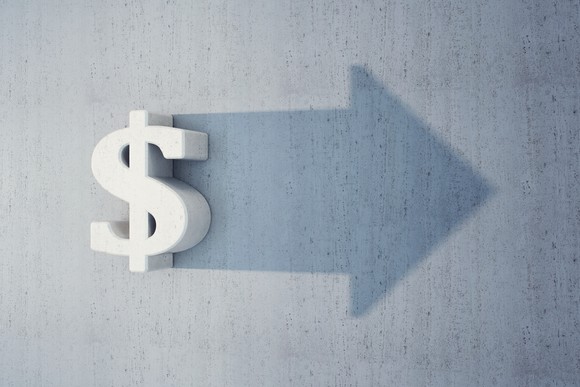 Dollar sign and a silhouette right-pointing arrow against a concrete wall.