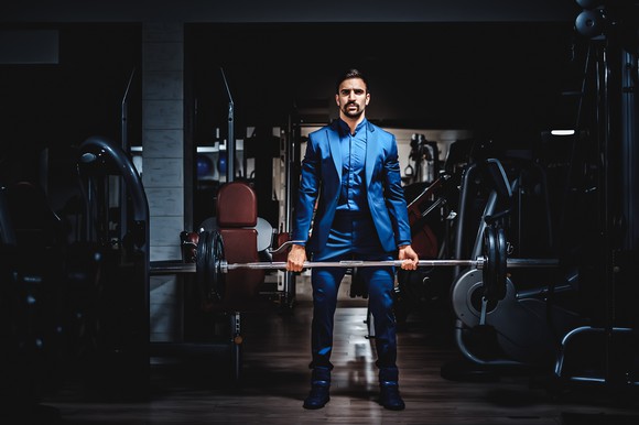 A man in a business suit lifts a barbell in a gym.