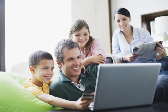 Family huddled around laptop looking at screen smiling.