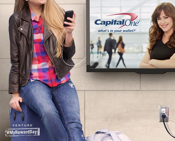 Person charging phone next to Capital One ad in an airport