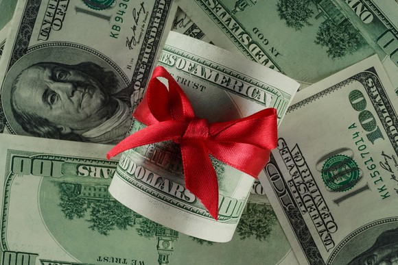 Roll of hundred-dollar bills wrapped in a red ribbon tied in a knot.
