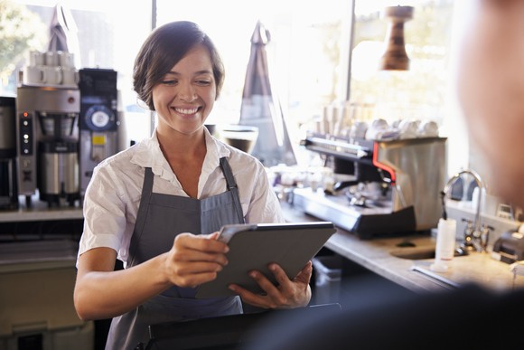 A smiling barista uses a tablet at point of sale.