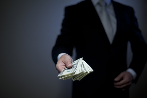 A person in a suit handing over a stack of cash.