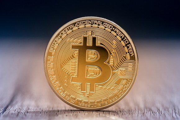 A physical gold bitcoin standing on a table.