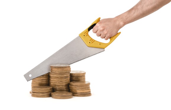 Hand holding a saw attempting to cut through a pile of gold colored coins