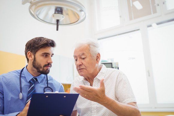 senior man talking to doctor holding clipboard medical expenses healthcare hospital