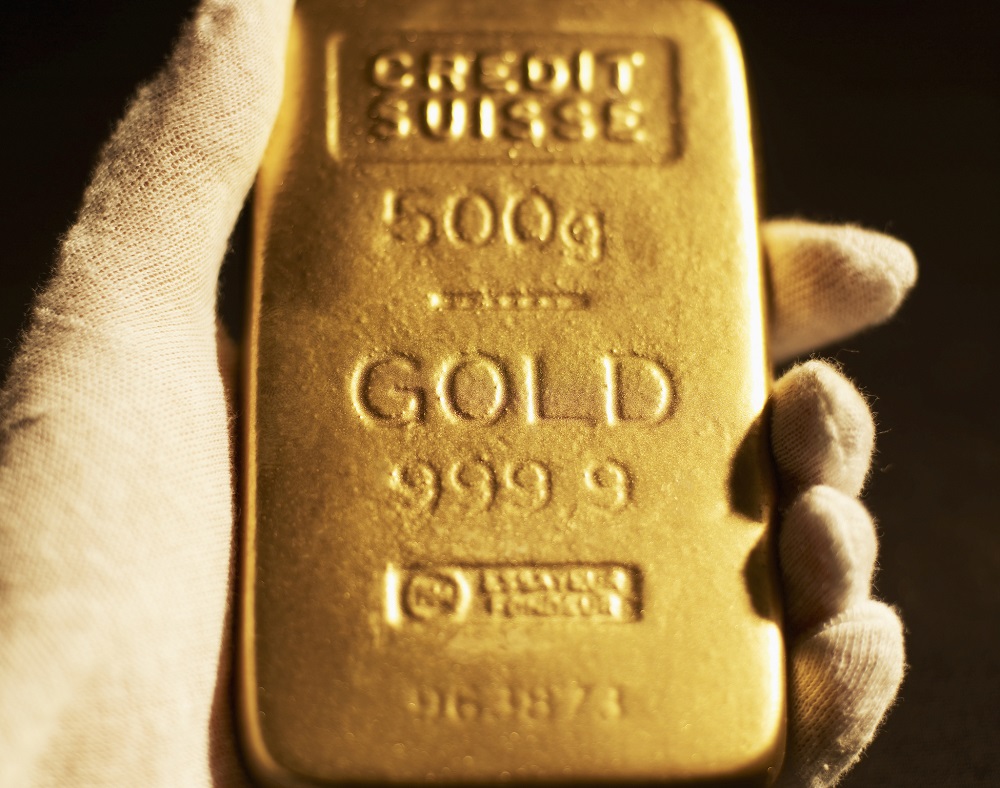 A gloved hand holding a gold bar