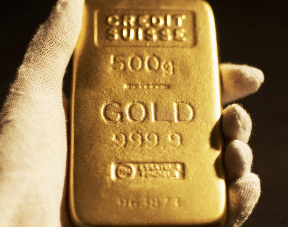 A gloved hand holding a gold bar