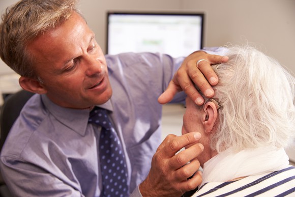 A man fits an elderly woman with a hearing aid.
