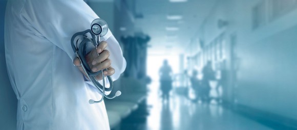 Medical professional in hospital hallway holding stethoscope.