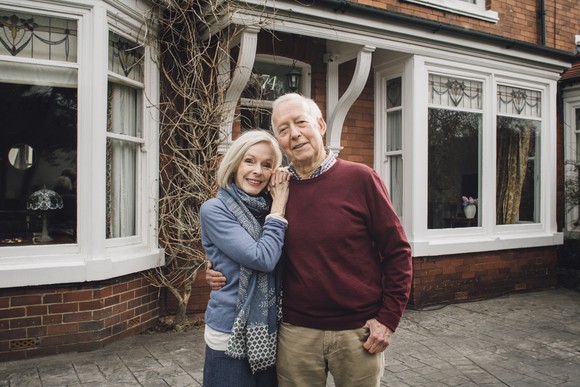 senior man and woman smiling and holding each other in front of a house