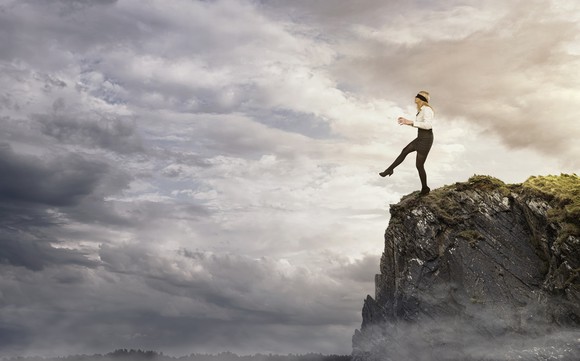Woman with a blindfold on stepping off a cliff.
