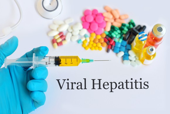 Gloved hand holding syringe by pile of pills over words Viral Hepatitis