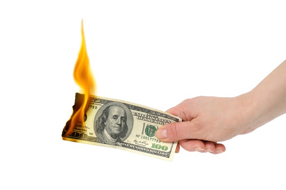 A hand holding a $100 billion that's on fire at the other end.