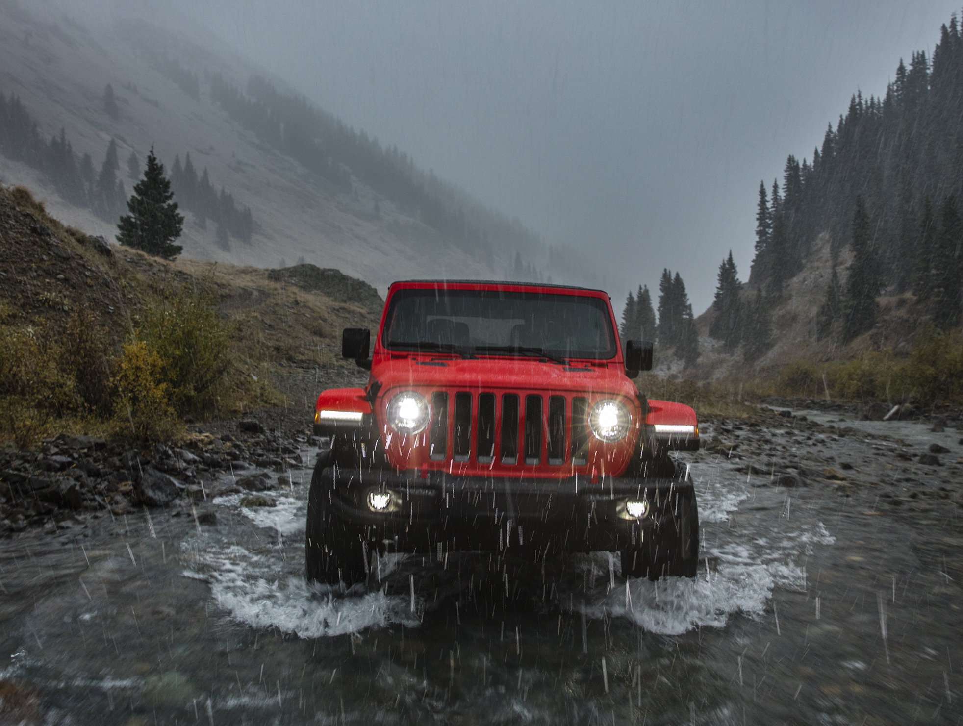 A red 2018 Jeep Wrangler fording a river in the mountains.