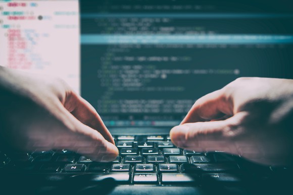 Hands typing on a laptop with code on the screen.