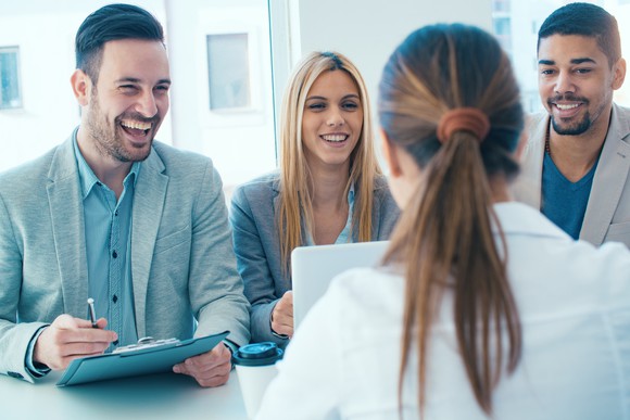 Three businesspeople laughing facing another businessperson across a table.
