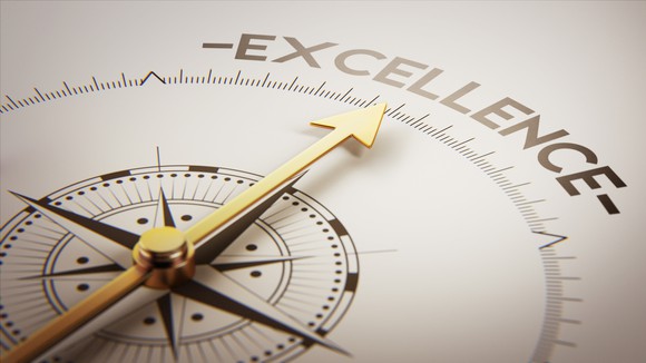 A compass face with the arrow pointing to a sign reading excellence.