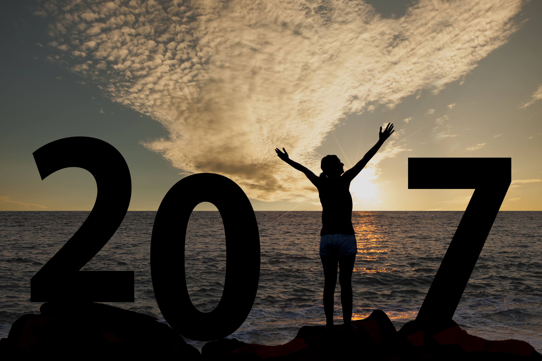 A woman in silhouette, standing with her arms raised overlooking the ocean, positioned as the 1 in 2017.