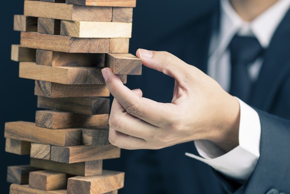 Picture of a business man precariously close to causing a large structure of wood blocks to come tumbling down.