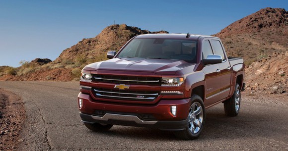 A red Chevrolet Silverado parked on a street with small mountains in the background.