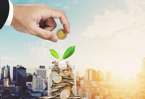 Picture of a businessman's hand placing another coin in a jar.