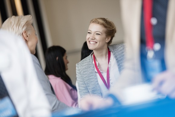 Smiling woman wearing a badge, talking to another woman